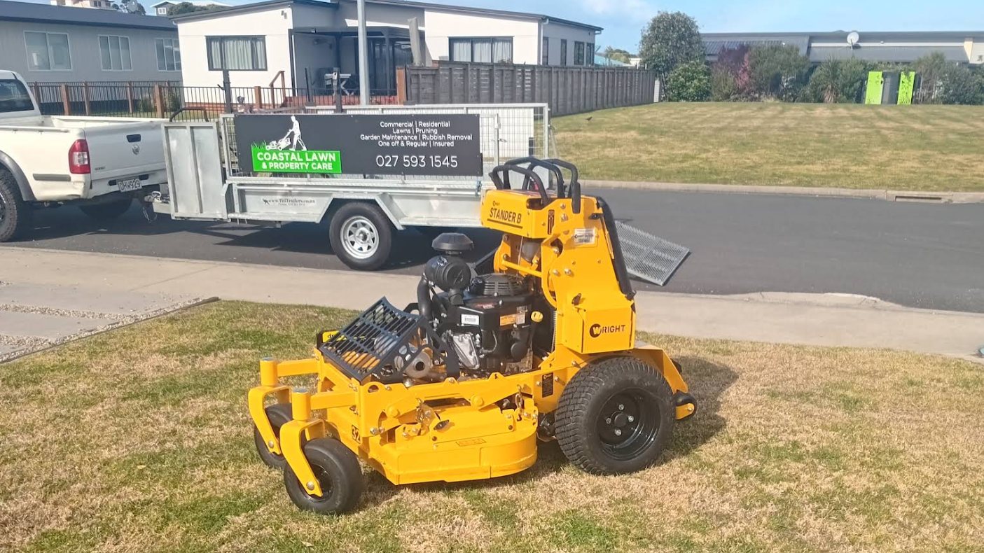 Coastal Lawn & Property Care mower and signwritten trailer parked on a Waihi lawn
